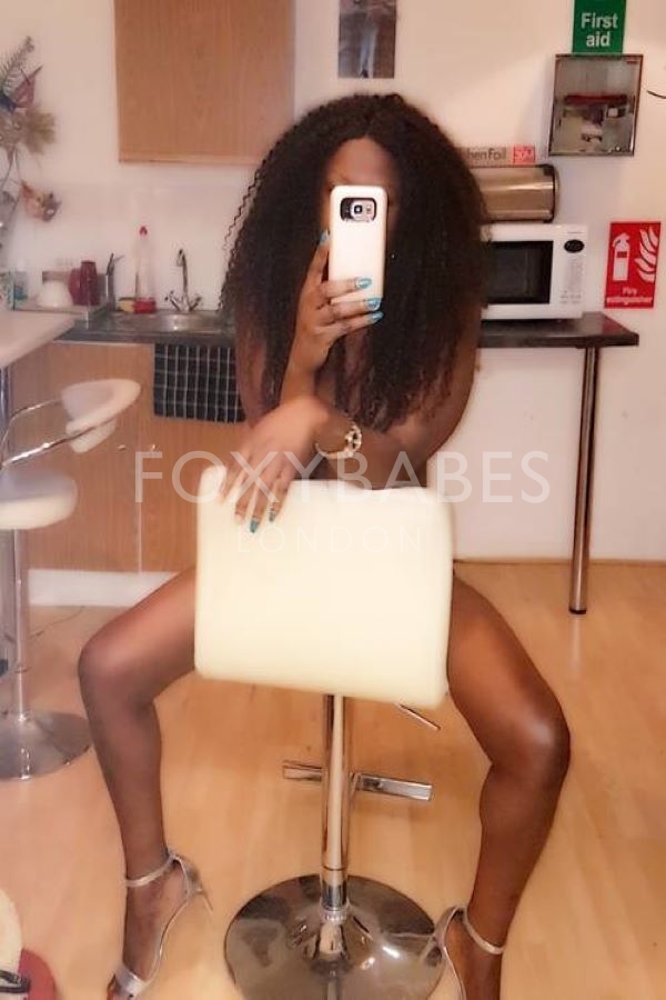ebony escort taking selfie on chair 
